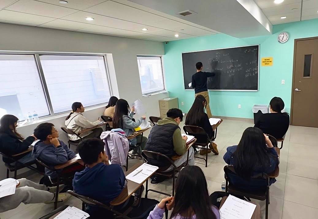 Experienced teacher explaining math concepts on the blackboard in a bright classroom